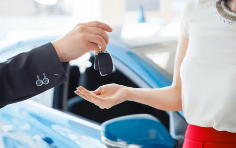 Being handed new car keys with blue car in background