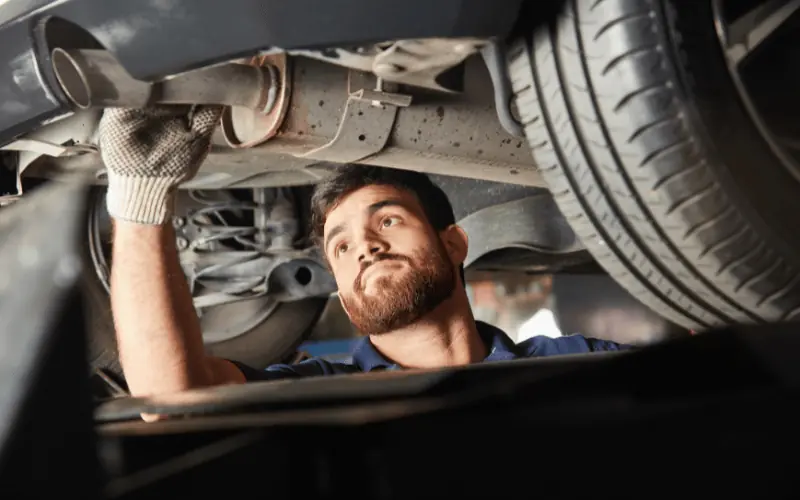 Mechanic performing vehicle inspection under car at garage
