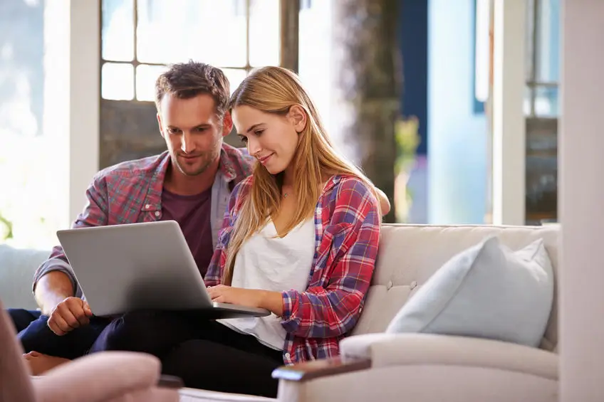 Couple sitting on sofa looking at laptop computer