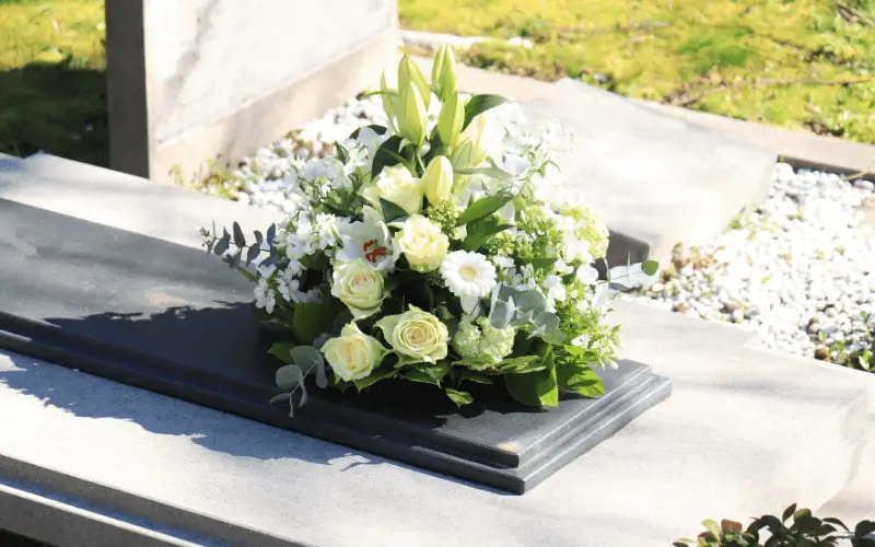 White and yellow funeral flowers sitting on grave stone