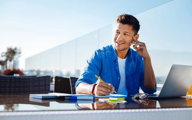 young man working remotely with laptop and notes on rooftop terrace in Spain