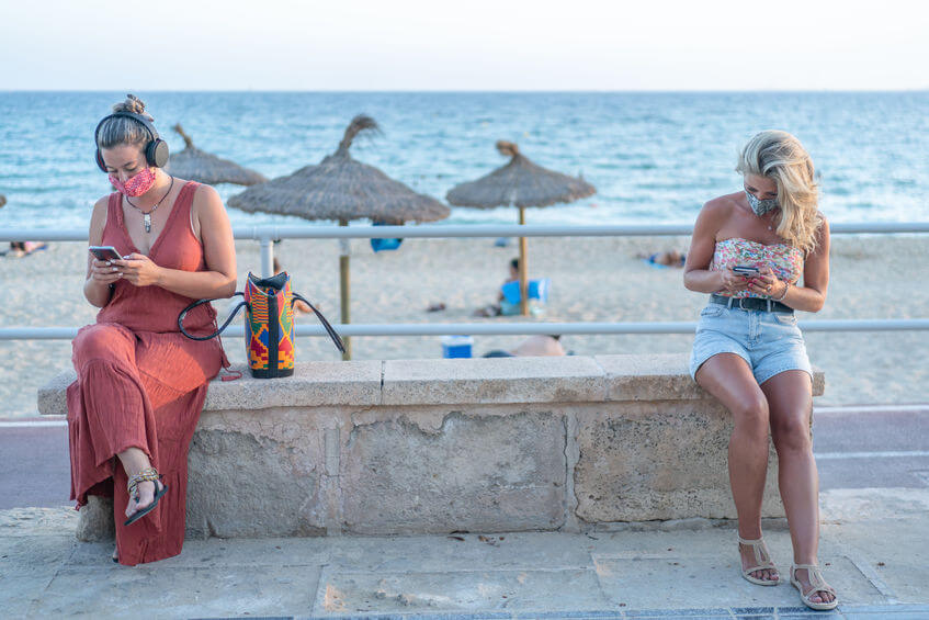 Tourists at beach wearing masks and on phones